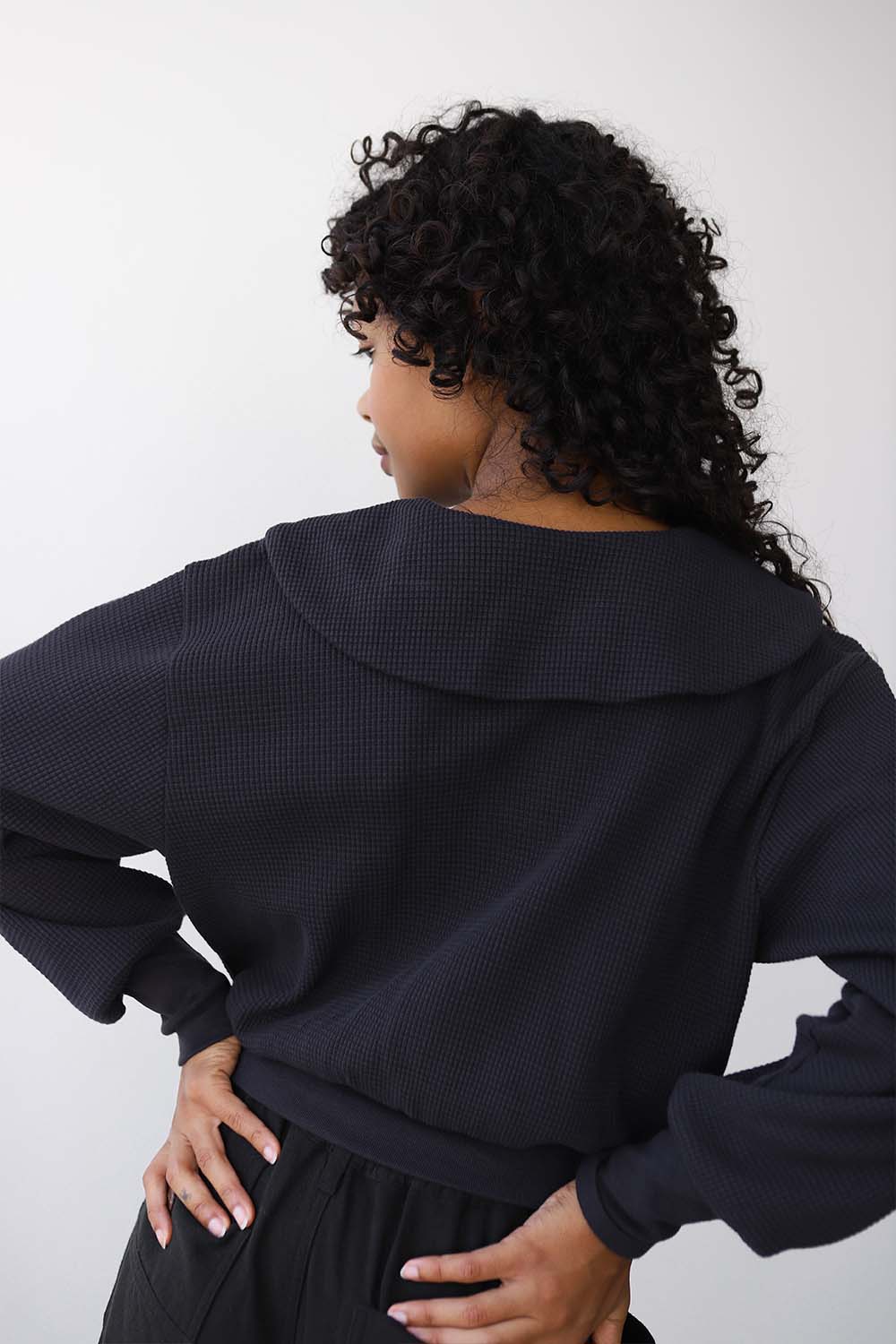 Woman wearing a black sailor inspired waffle cardigan with their back to the camera on a white background