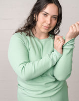Woman wearing an organic waffle thermal top in sage, pulling her sleeve. 