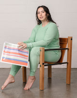 Woman wearing organic waffle thermal pajamas, sitting in a vintage modern chair and reading the newspaper.