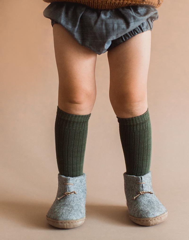 Baby's legs wearing green knee socks and grey wool Glerups baby boots
