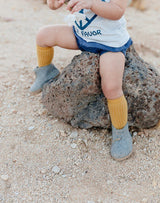 Baby sitting on a rock wearing mustard knee socks and grey Glerups wool baby boots