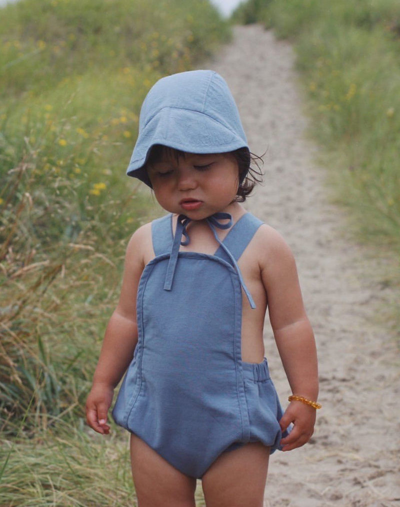 Baby wearing moon blue brimmed bonnet and moon blue sun suit
